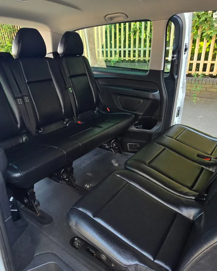 Interior of the 8-seater van seen through the open side door, with black leather passenger seats
